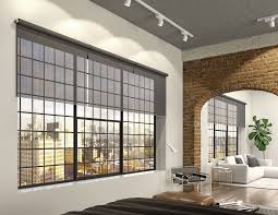 Modern loft apartment with large grid windows, gray roller blinds, exposed brick walls, and a cozy seating area.