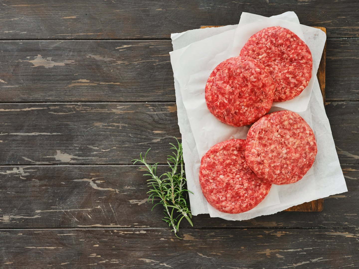 Four fresh raw burger patty or ground beef meat burger steak cutlets on dark wooden background. Top view.