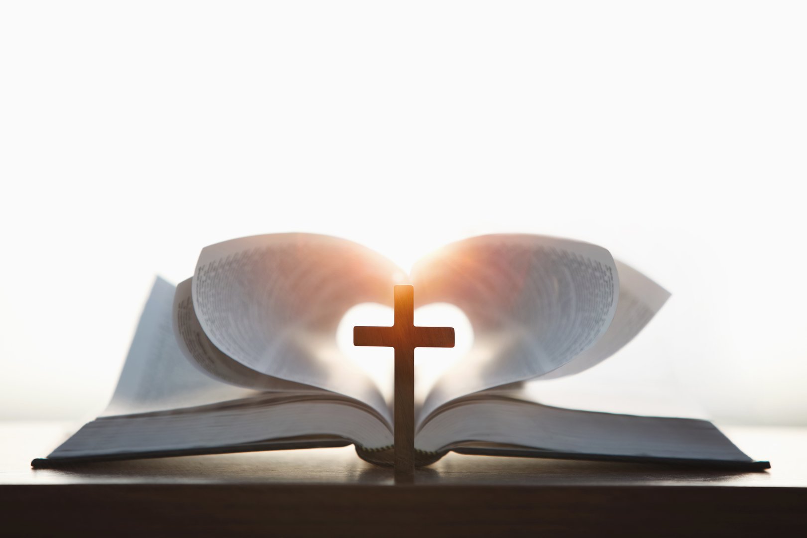 A cross symbolizing the death and resurrection of Jesus and a brightly lit heart-shaped Bible, the love of Jesus Christ in the background
