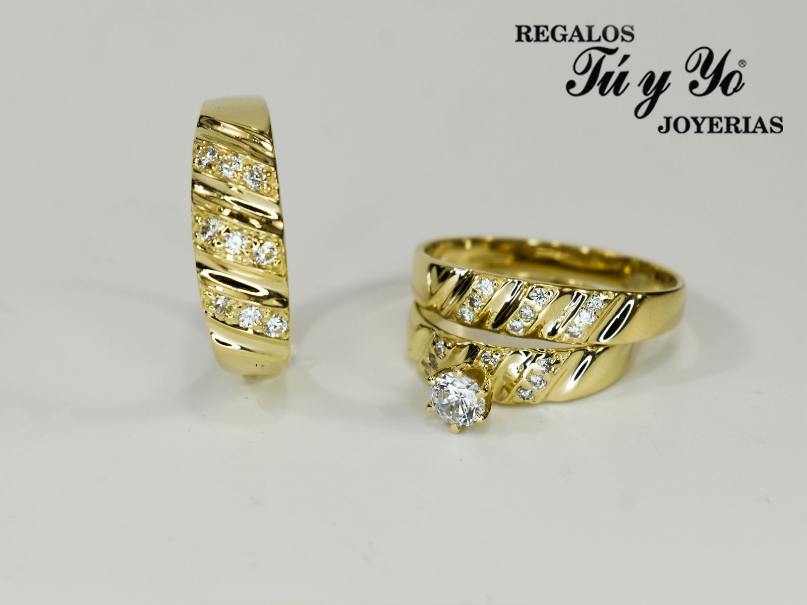 Gold rings with diamond accents displayed against a white background, featuring "Regalos Tú y Yo Joyerías" text.