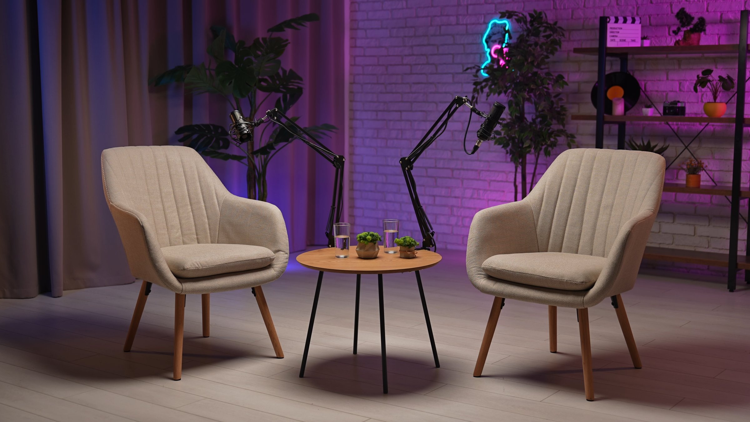 Two stylish chairs await an engaging dialogue in a contemporary podcast studio. The inviting atmosphere is enhanced by soft lighting, a recording setup, and personal touches, perfect for storytelling.