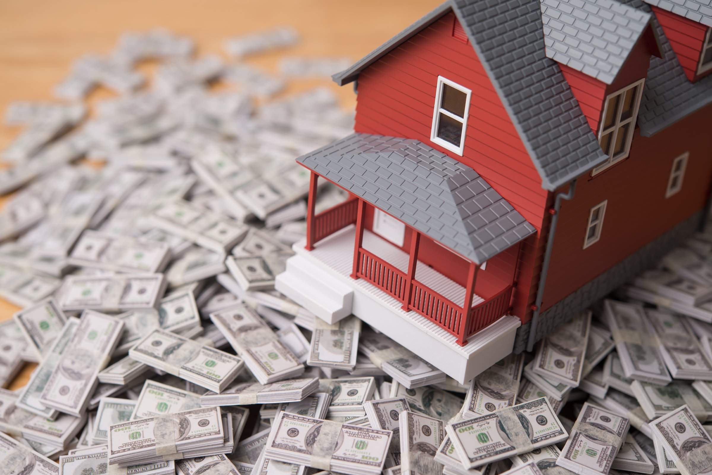 House model on heap US dollar banknotes. Return on investment (ROI) from real estate investment trust (REIT), yield and profit from sales or rentals, reverse mortgage, home for cash and so on concept.