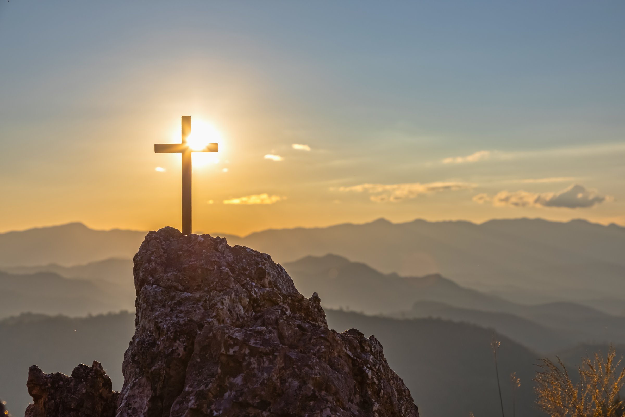 Silhouettes of crucifix symbol on top mountain with bright sunbeam on the colorful sky background