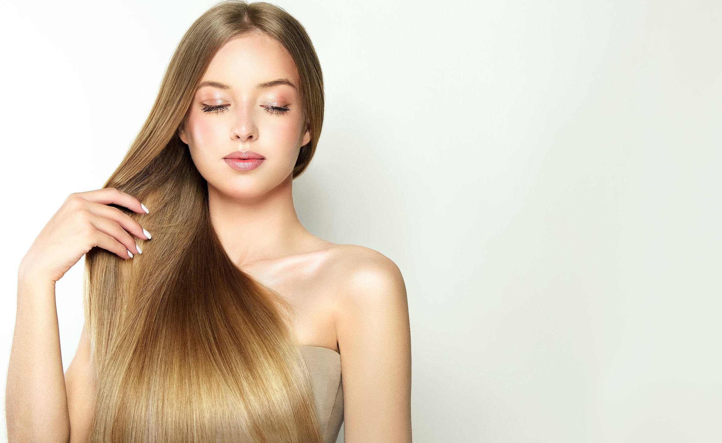 Graceful fingers with pale rose manicure is touching own straight hair in a natural color.Portrait of beautiful woman dressed in elegant soft makeup. Model with gray eyes. Hairstyling manicure makeup.