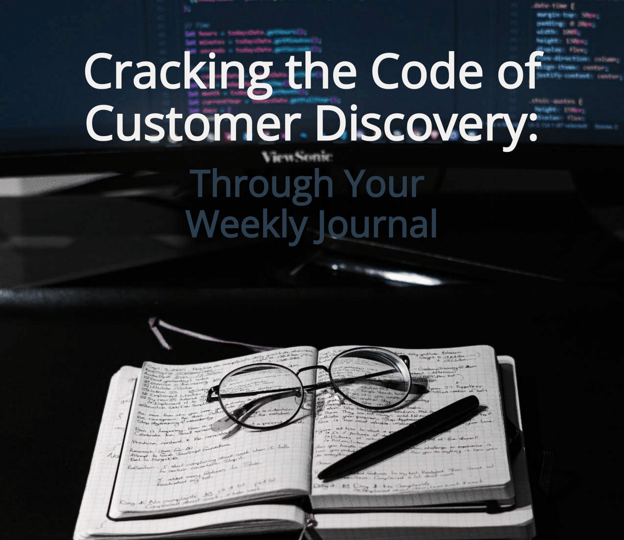 Open notebook with glasses and pen on a desk in front of a computer screen displaying code, with text about customer discovery.