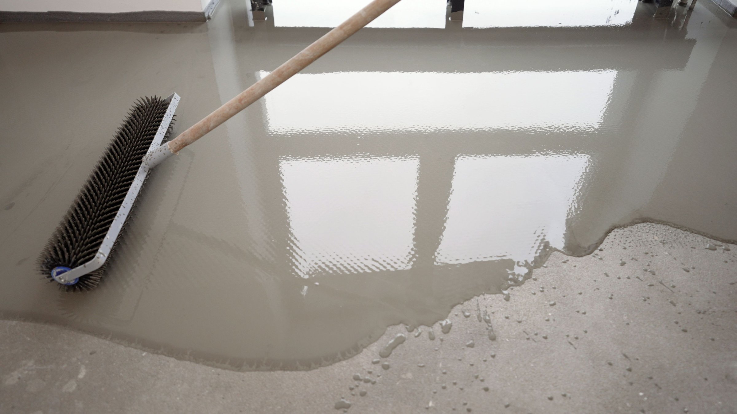 Worker using a spiked roller to level and smooth a concrete surface, ensuring a flat and even finish