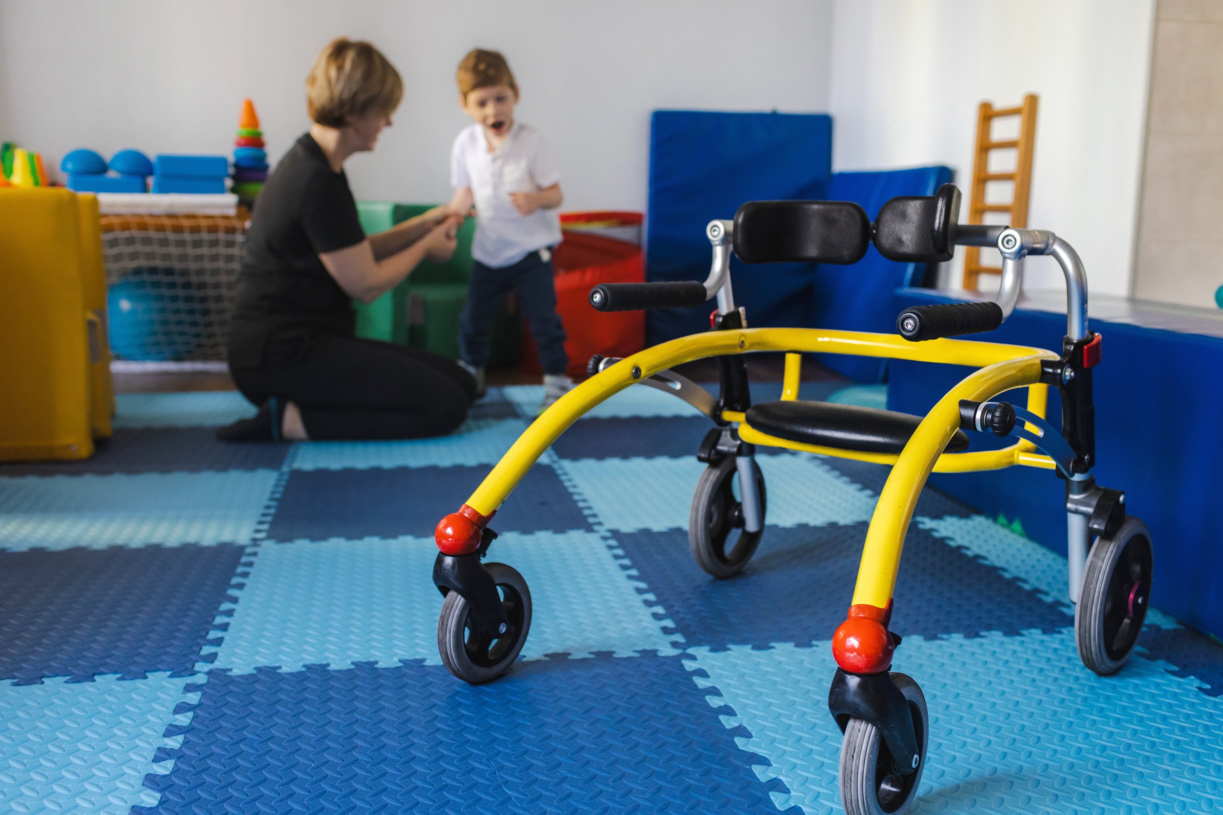 Young boy with cerebral palsy participates in physical therapy assisted by a therapist in a vibrant rehabilitation environment using open frame walker