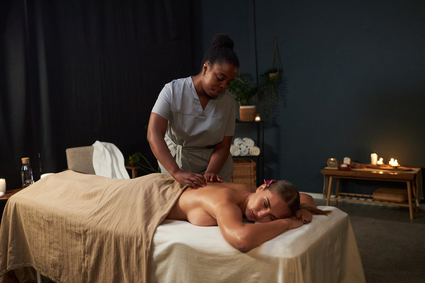 Woman receiving relaxing back massage from a professional masseuse in a tranquil spa environment with candles and soft lighting creating calming atmosphere