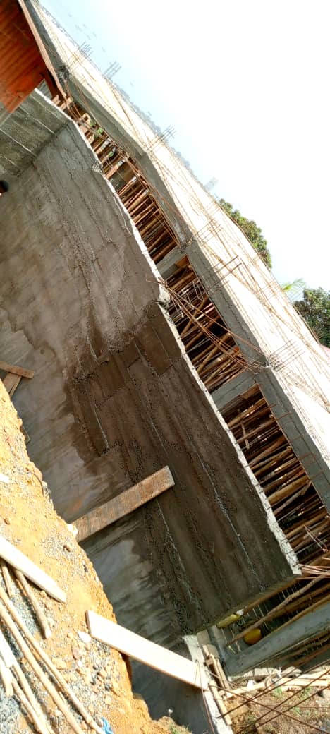 Construction site with concrete walls and wooden scaffolding, showing a large unfinished building structure.