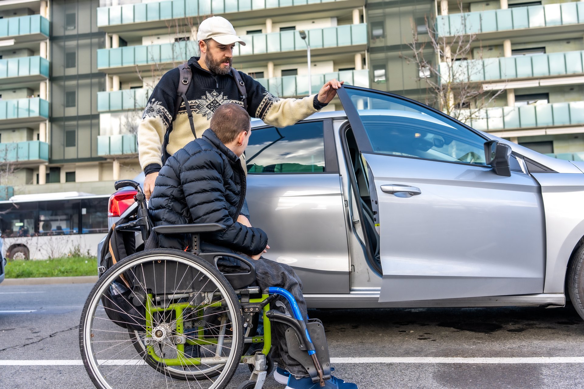 Man helping friend with disability get out of car and into wheelchair