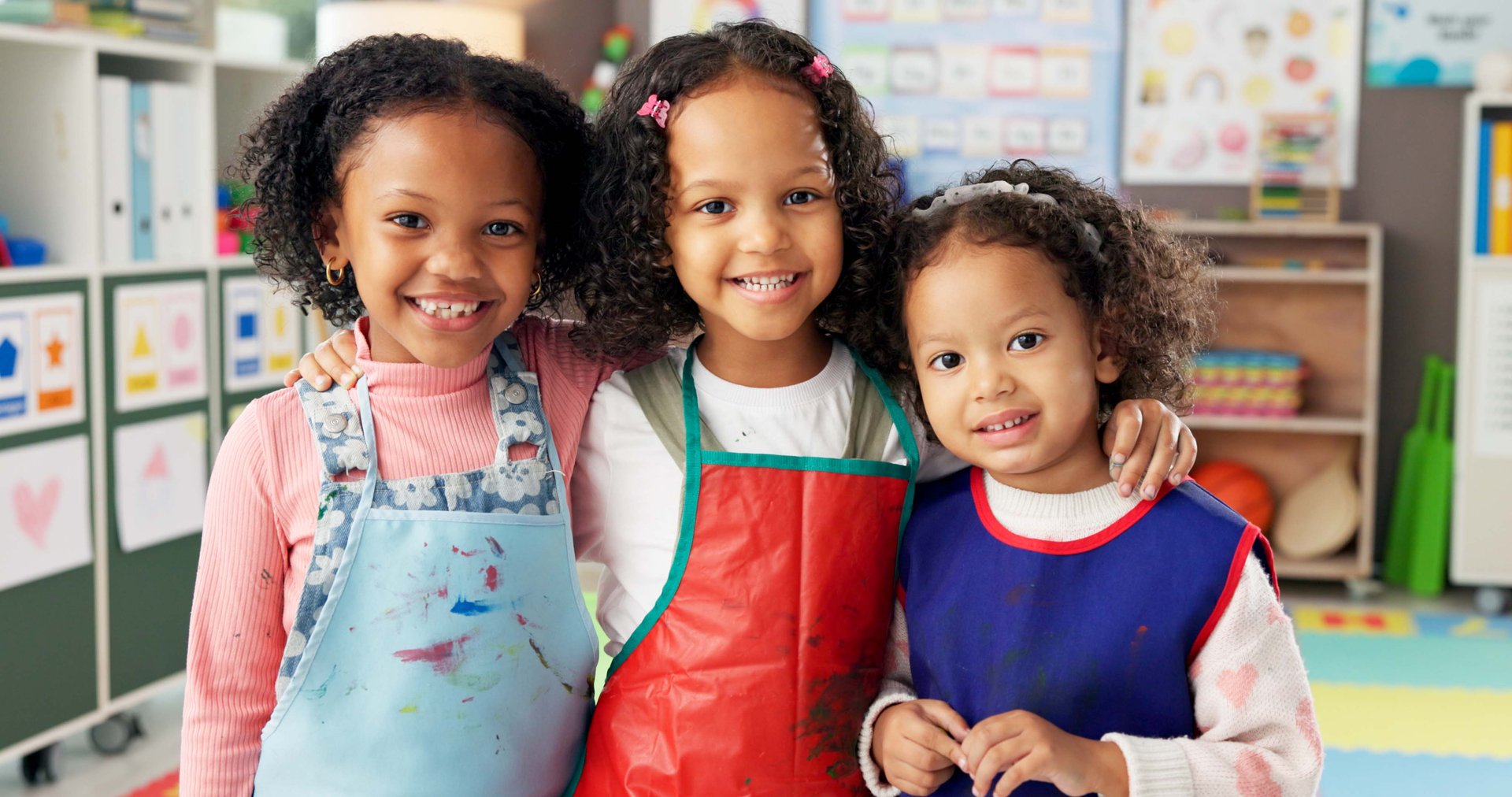 Happy girls, portrait and kindergarten with hug for friendship, education or fun learning together. Face, kids or children with smile or apron for creativity, art and crafts in elementary classroom