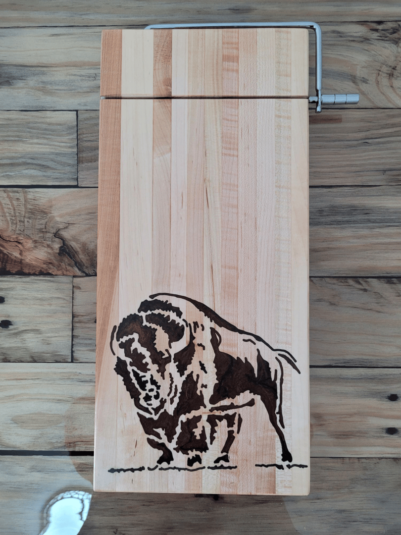 Wooden cutting board with an engraved bison design, featuring a metal clamping mechanism. Set on a wood-textured background.