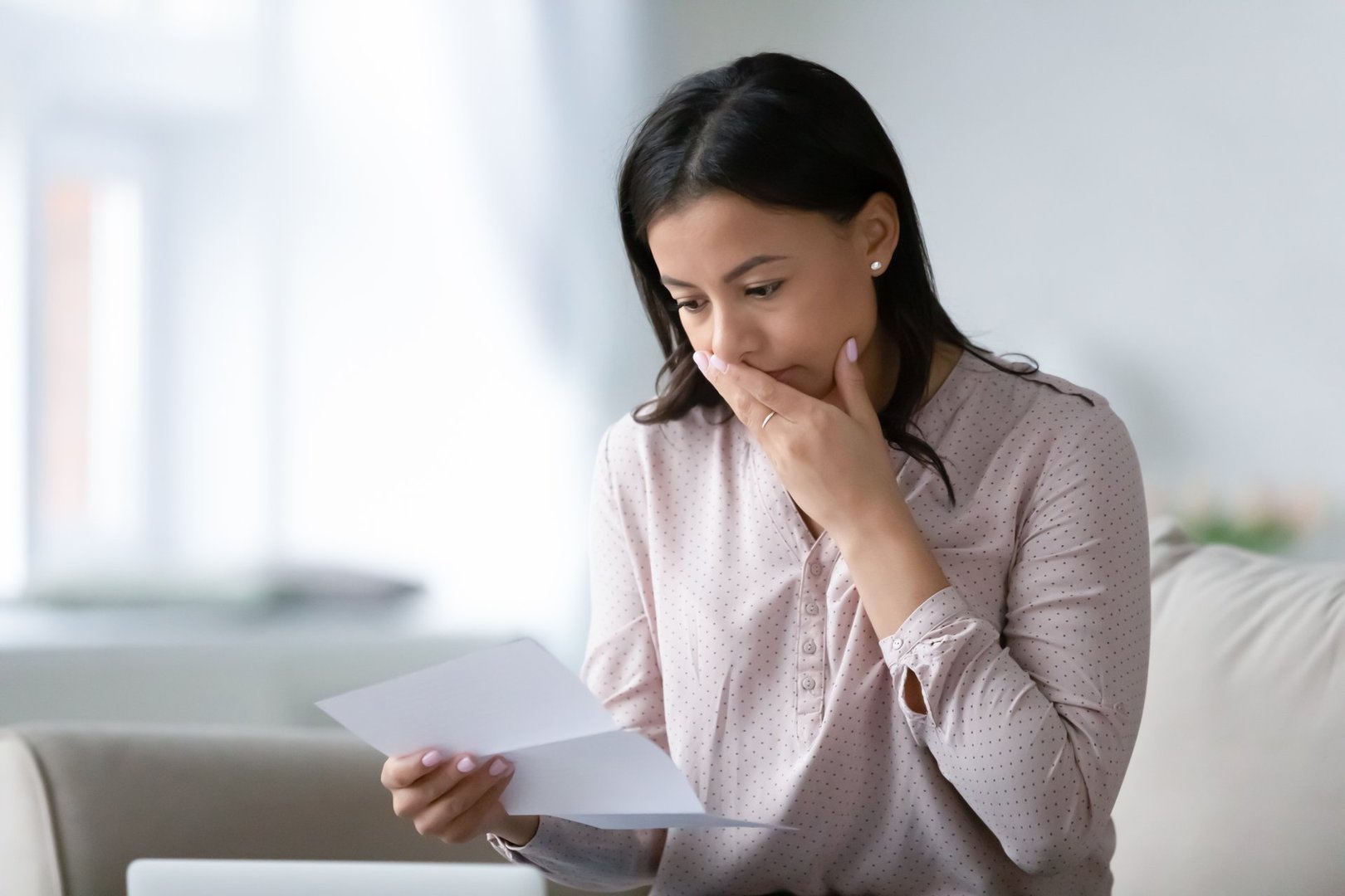 Distressed African American young woman sit on couch at home read bad negative news in paper correspondence, unhappy biracial female stressed consider unpleasant message in postal letter