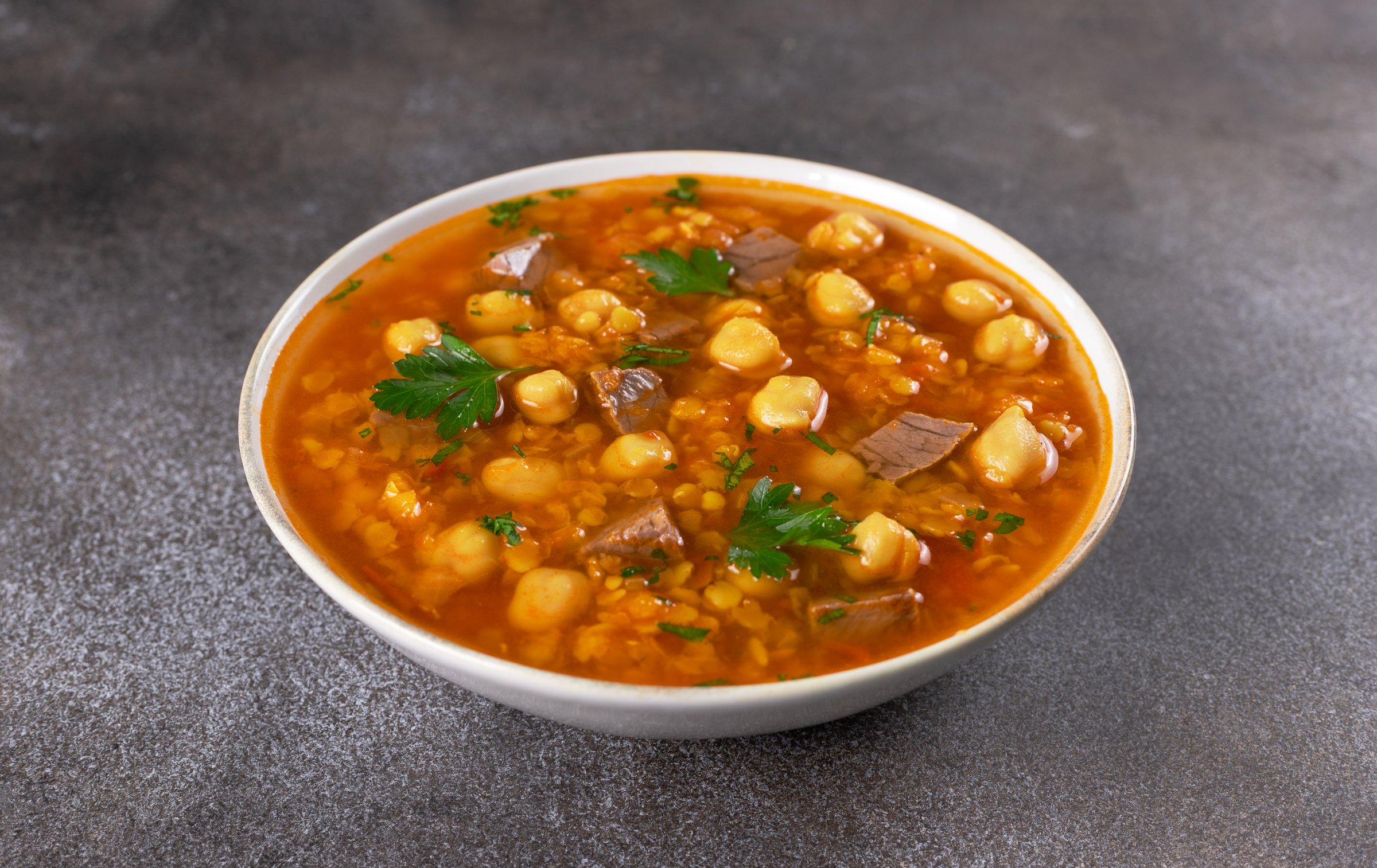 Bowl of Moroccan harira soup with chickpeas, beef, lentils and fresh parsley on grey background. Middle East cuisine. High quality photo