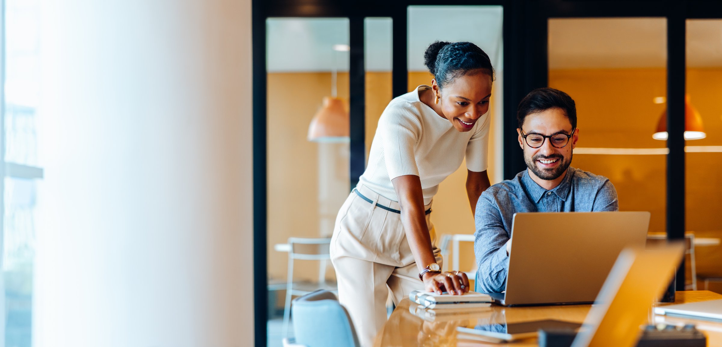 Two colleagues, one female and one male, review work on a laptop screen at an office. They appear to be collaborating effectively while sharing ideas and working towards completing a business project.