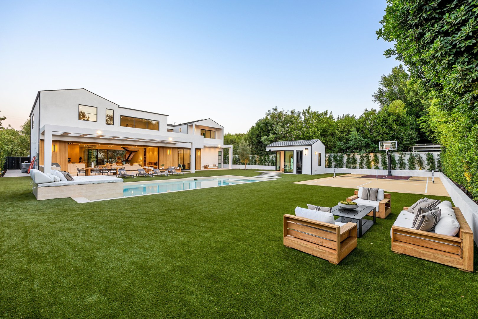 Modern luxury home with a spacious backyard, pool, and seating area under a clear blue sky.