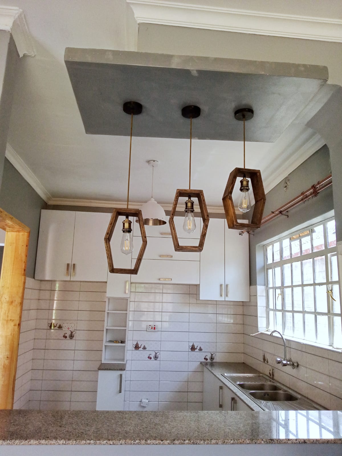 Modern kitchen with hexagonal pendant lights, white cabinets, tiled backsplash, and a large window over the sink.