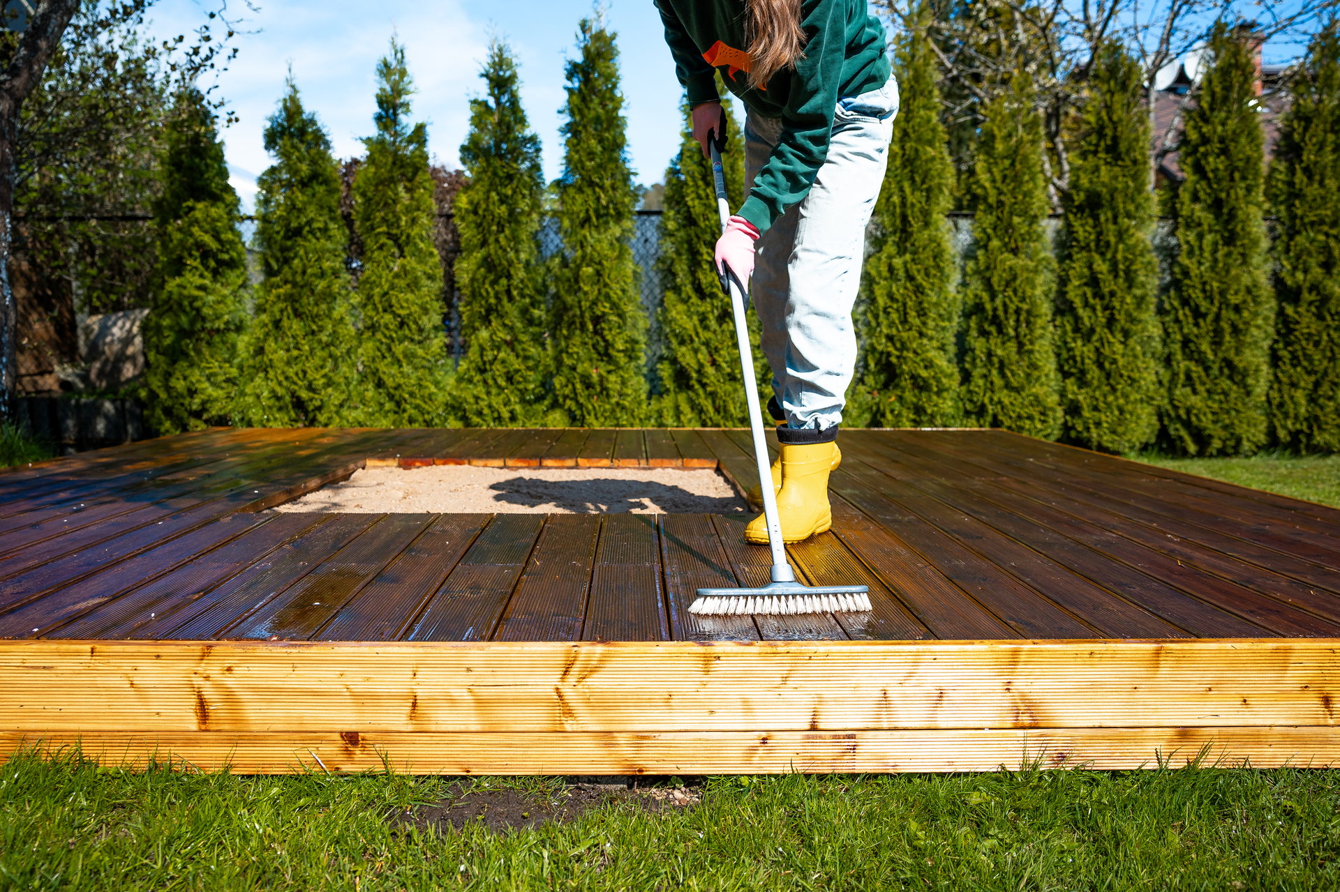 Cleaning a wooden deck with a scrub brush on a sunny day in the backyard