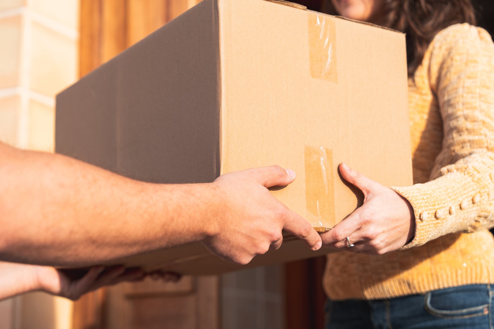 Detail shot of a cardboard box being passed between courier and customer during home delivery.