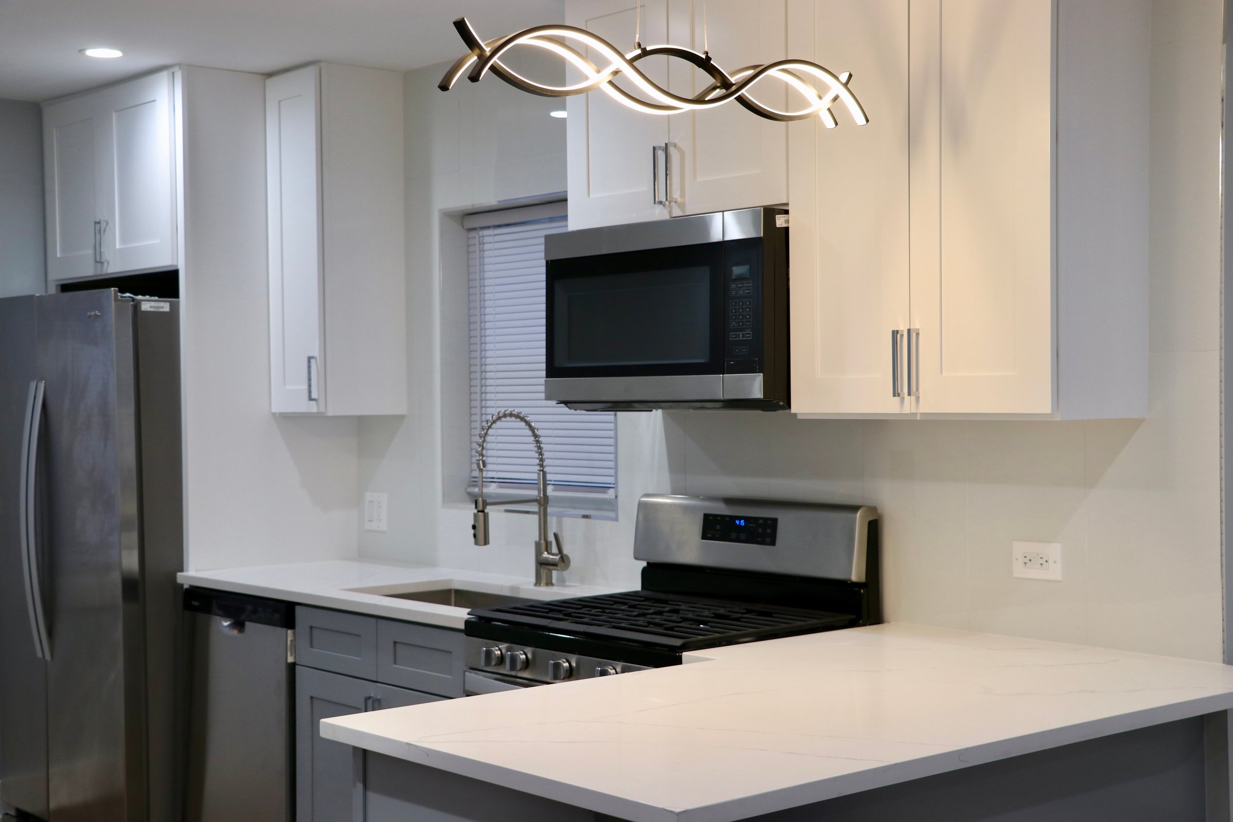 Modern kitchen with white cabinets, stainless steel appliances, and a sleek pendant light above a marble countertop.