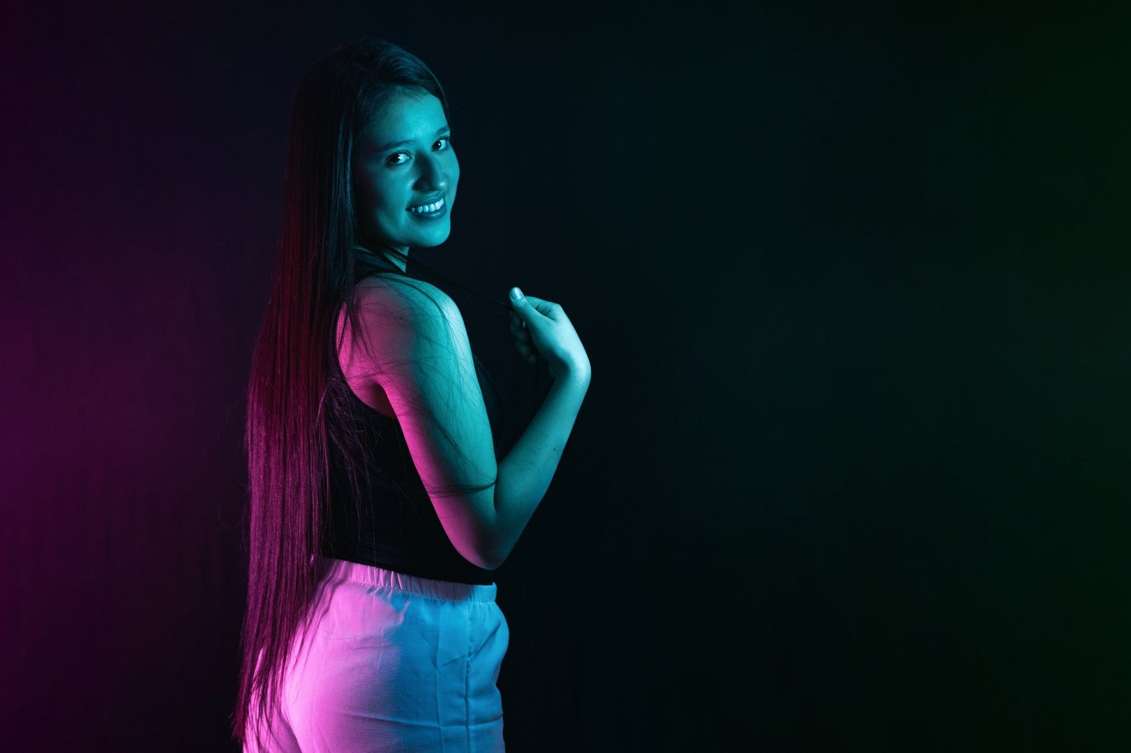 young latina woman smiling and looking sideways, being illuminated with purple and green studio lights.