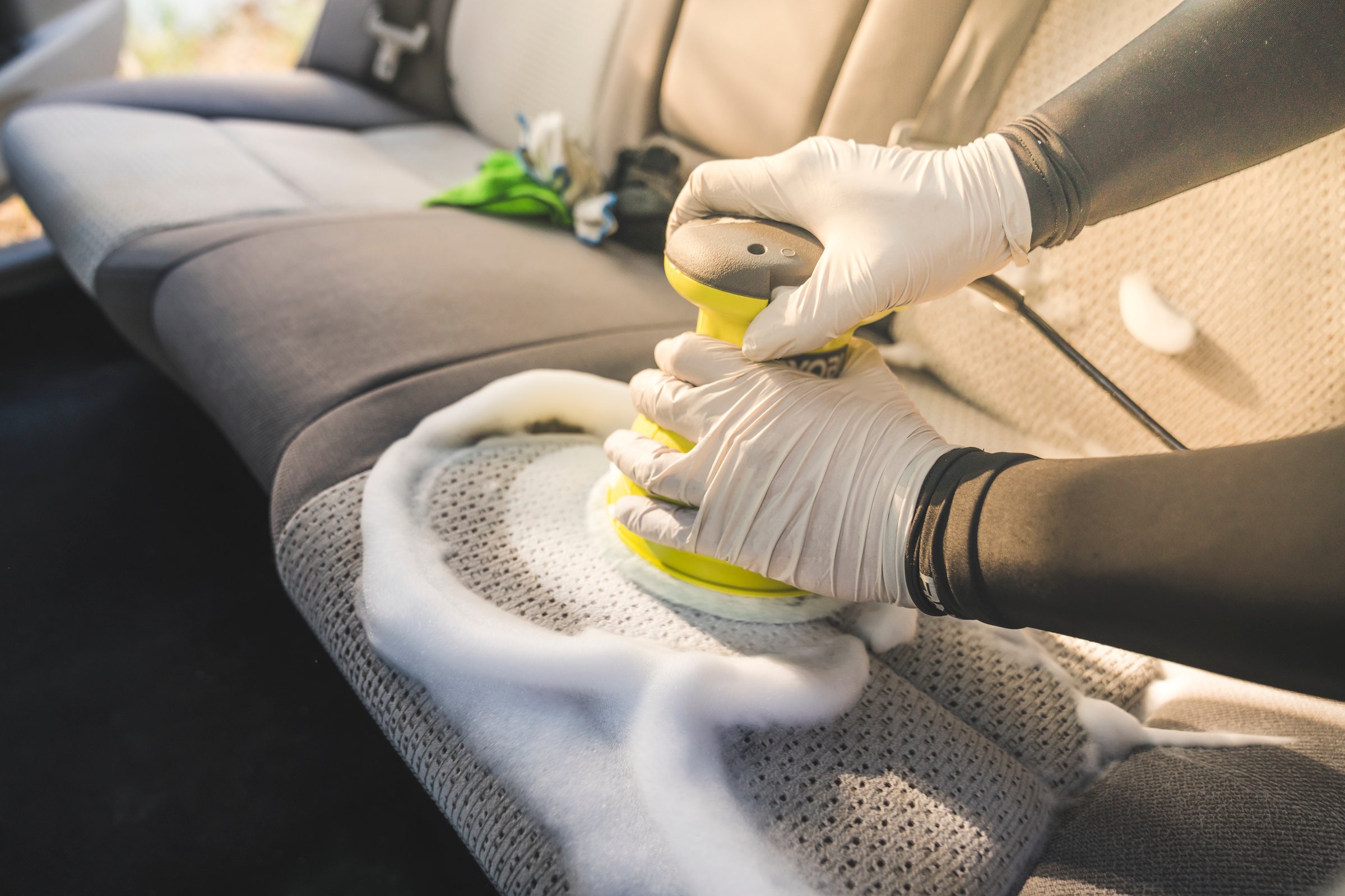 a man cleaning car interior by use foam chemical  and scrubbing machine.