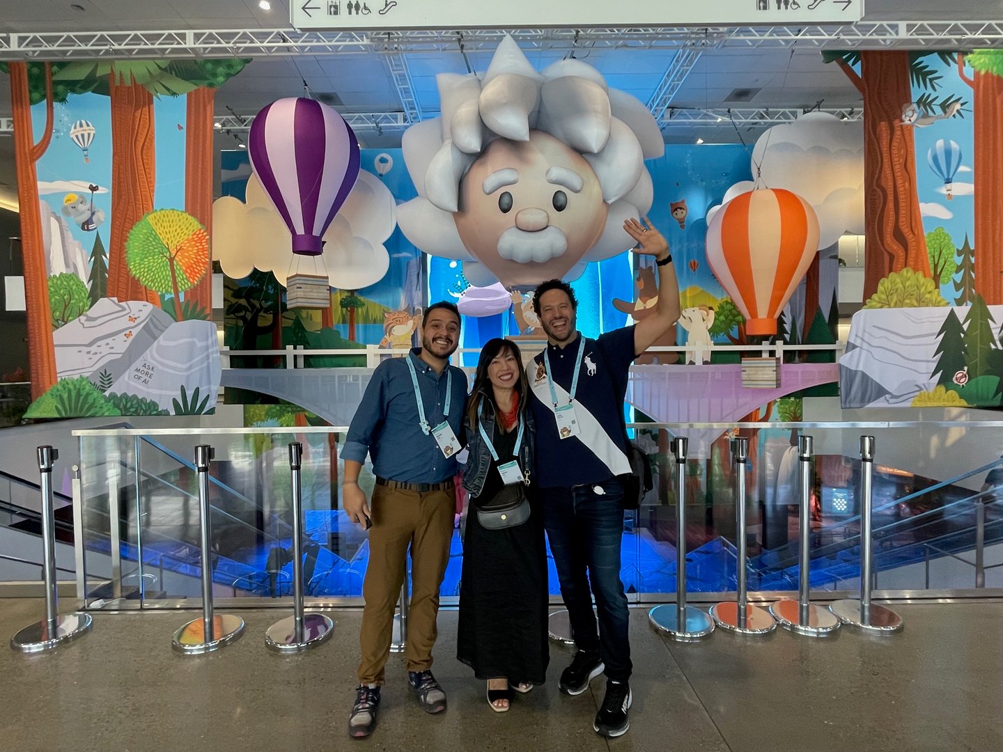 Three people posing in front of colorful balloons and a character backdrop at an event.