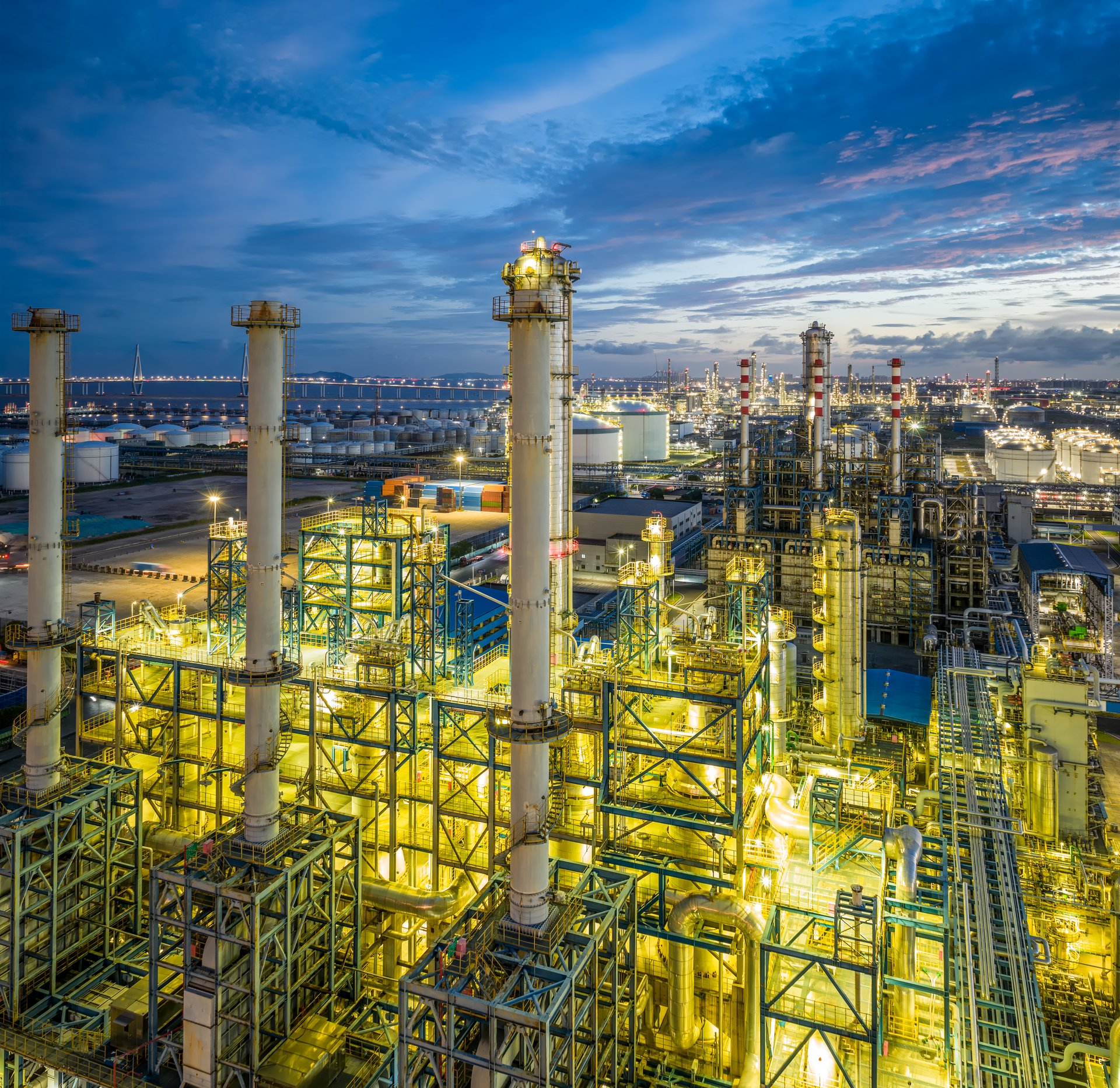 Intricate network of pipes and structures of a vast petrochemical complex illuminated against the evening sky.