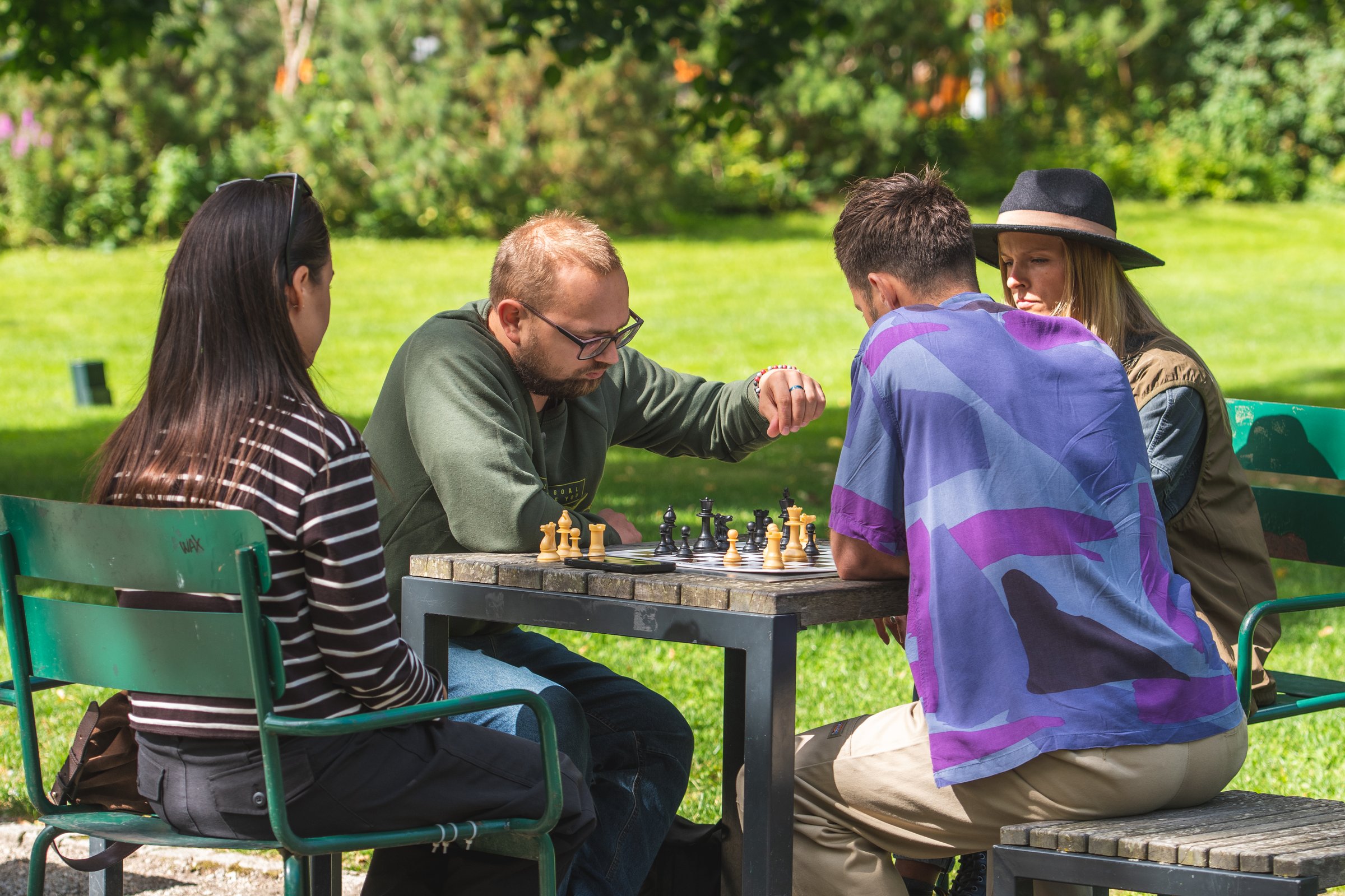 Group of friends playing chess outdoors in a park, enjoying leisure time together on a sunny day