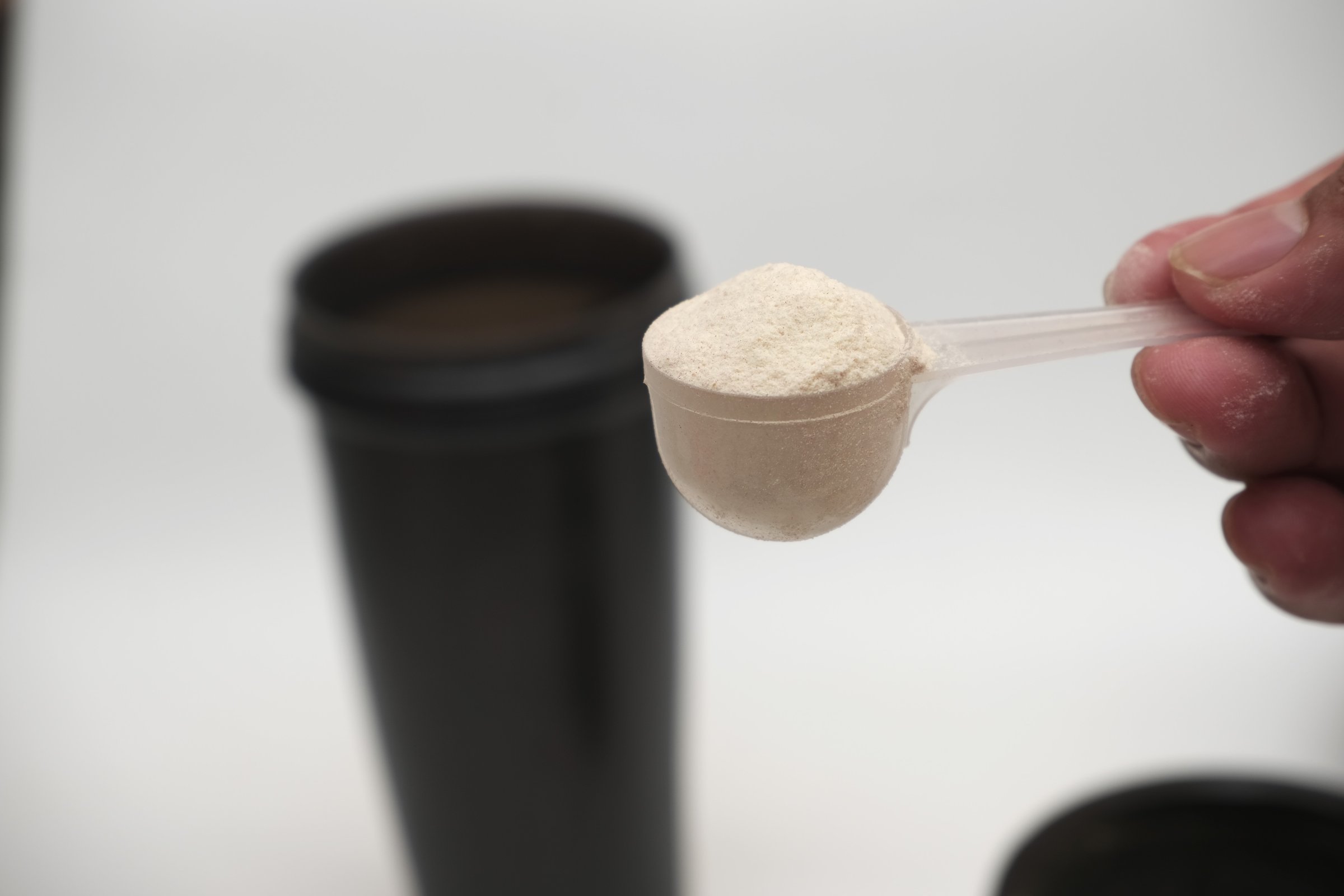 Close-up of a hand holding a scoop of creatine monohydrate powder taken from an open supplement container