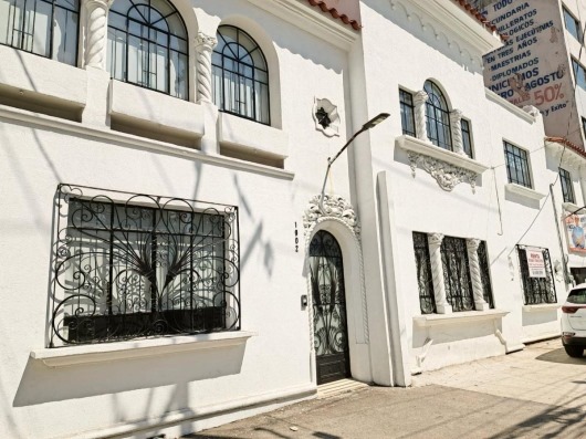 White stucco building with ornate wrought iron window grilles and decorative elements, seen on a sunny street.