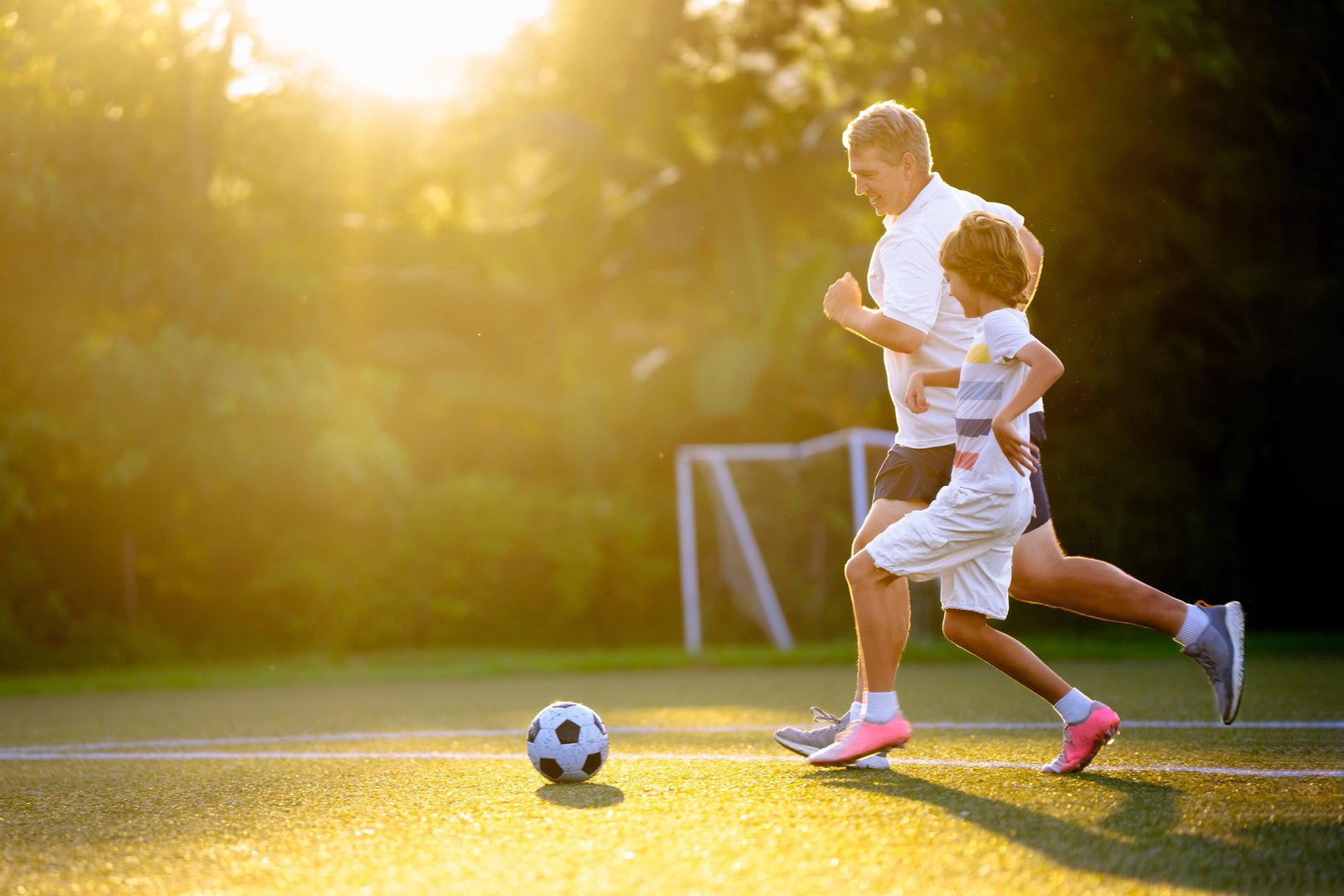 Child playing football. Kids play soccer on outdoor pitch. Little boy kicking ball in summer park. Healthy activity for young children. School sport club team. Football junior league.