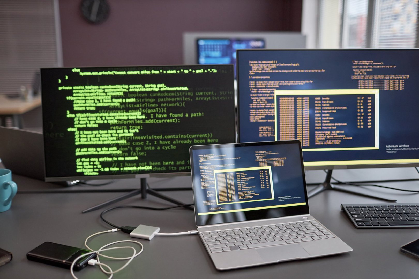 Background image of computers and laptops with green code lines on screen at workplace in IT development company