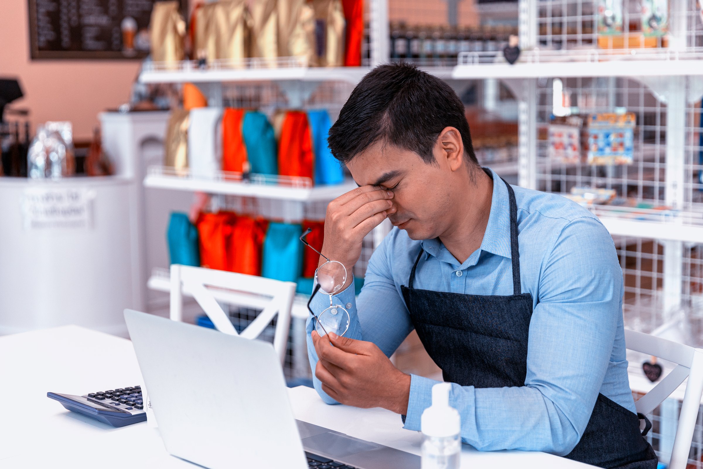 Young frustrated male owner uses computer and software to solve problems for his startup bakery or café shop. Shop owner gets tired at the end of the day and looks for inspiration through his laptop.