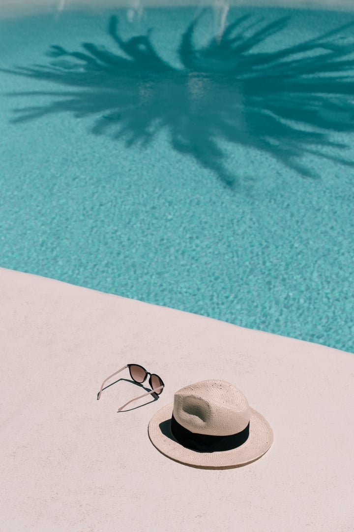 Straw hat, sunglasses at poolside. Summer vacation holidays. Swimming pool with a palm tree shadow