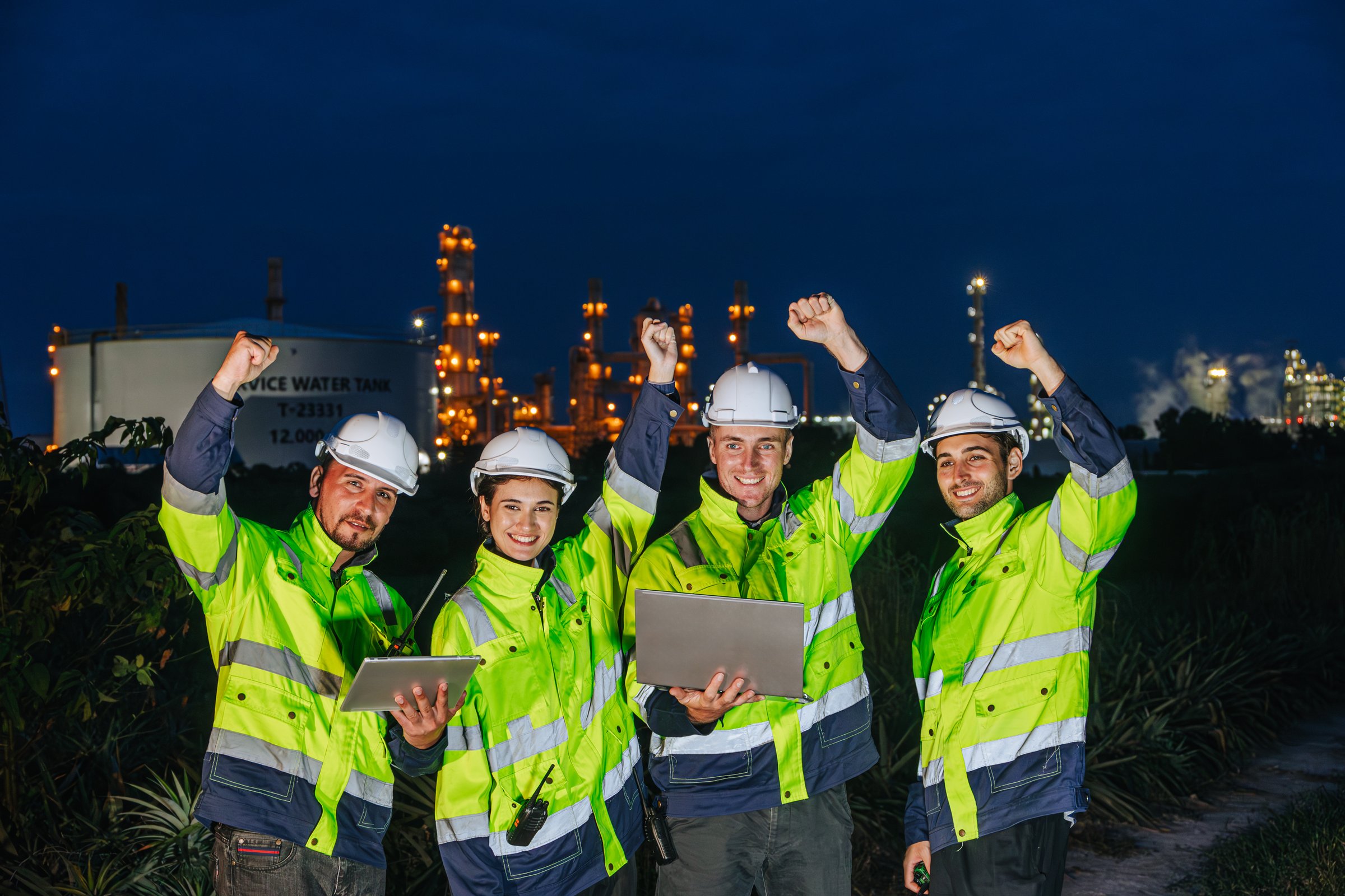 Group of Night Shift Oil And Gas Refinery Engineer Team Workers Cheerful Happy Greeting Finished Jobs Hand Rising Together In Petroleum Industry.