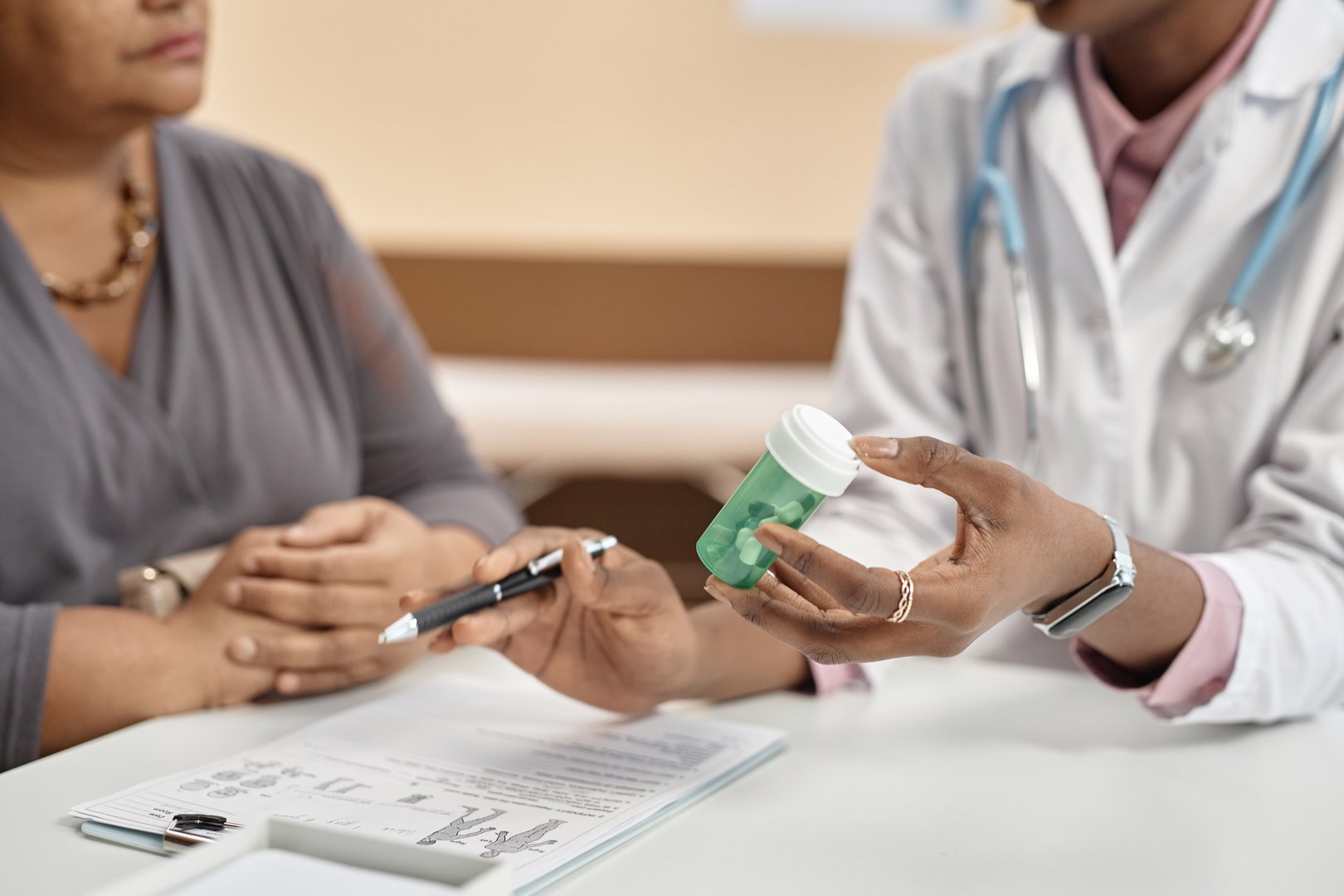 Close up shot of green plastic bottle with pills in hand of female doctor talking to patient during consultation in clinic
