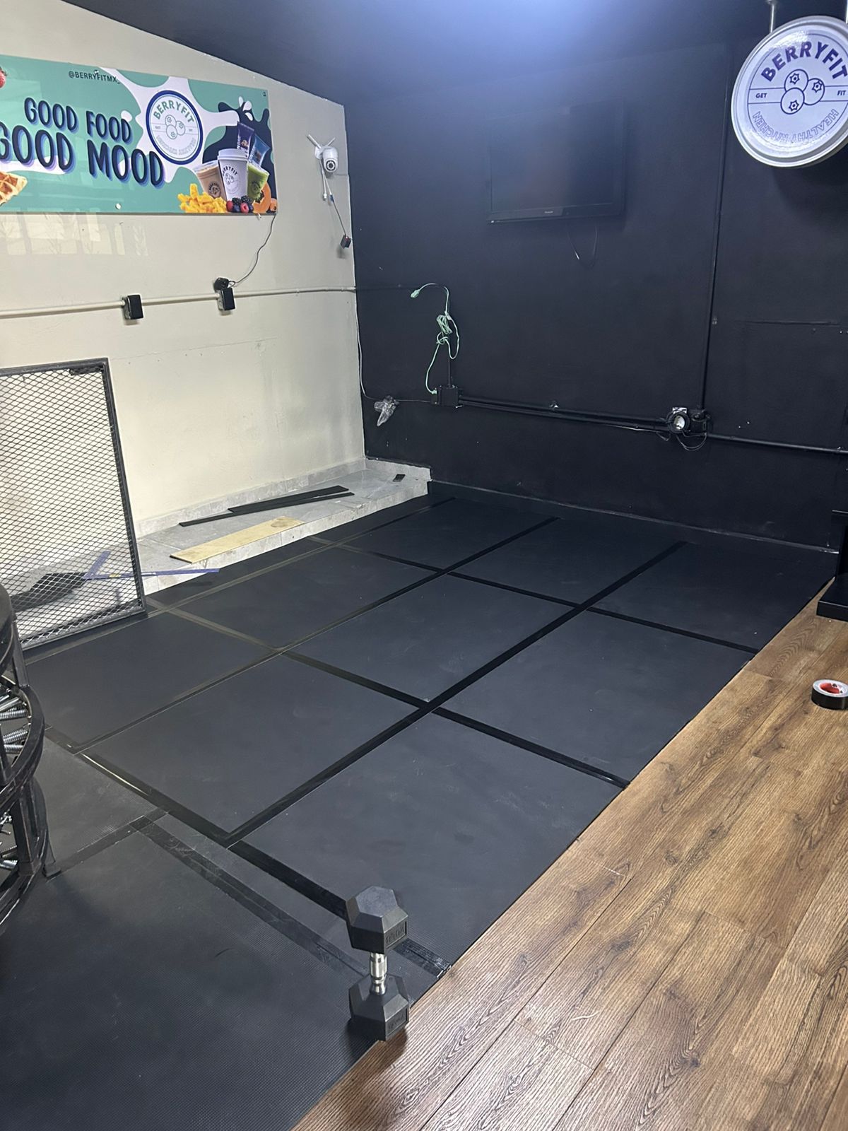 Empty workout space with black mats, a dumbbell, and a sign reading Good Food Good Mood on the wall.
