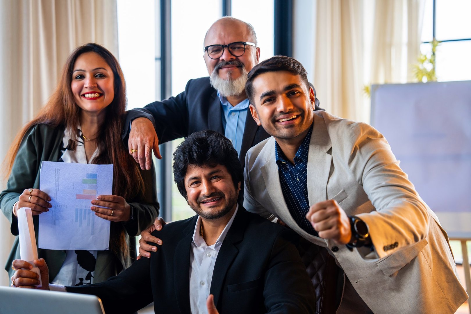 Indian Asian group of confident corporate professionals in formal attire working on laptop and celebrating success