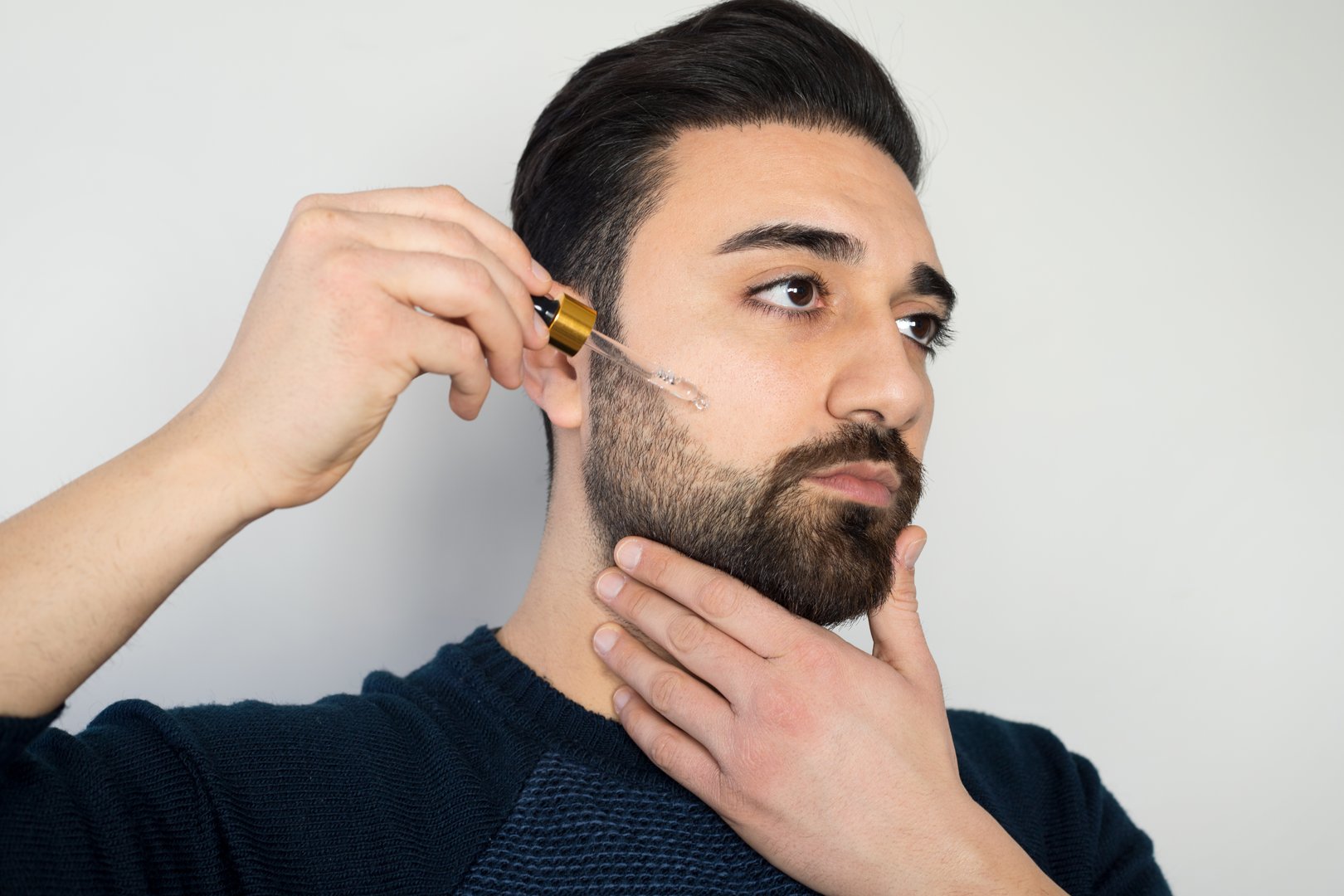 Bearded man holding pippete with beard oil