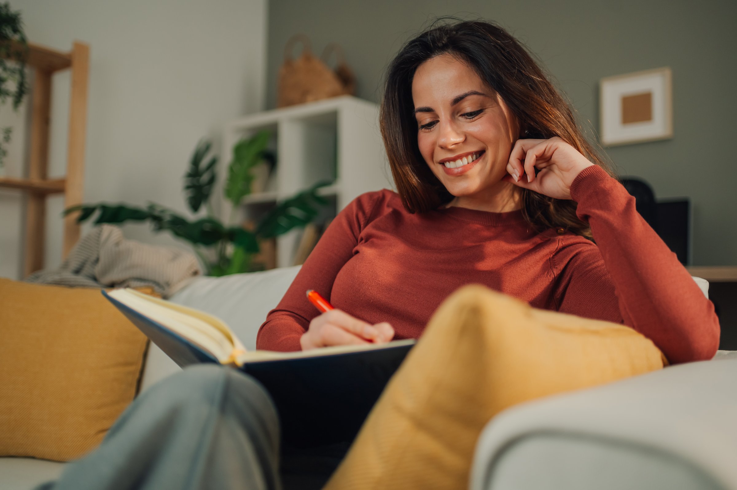 Young woman relaxing on the sofa at home and writing notes on a notebook