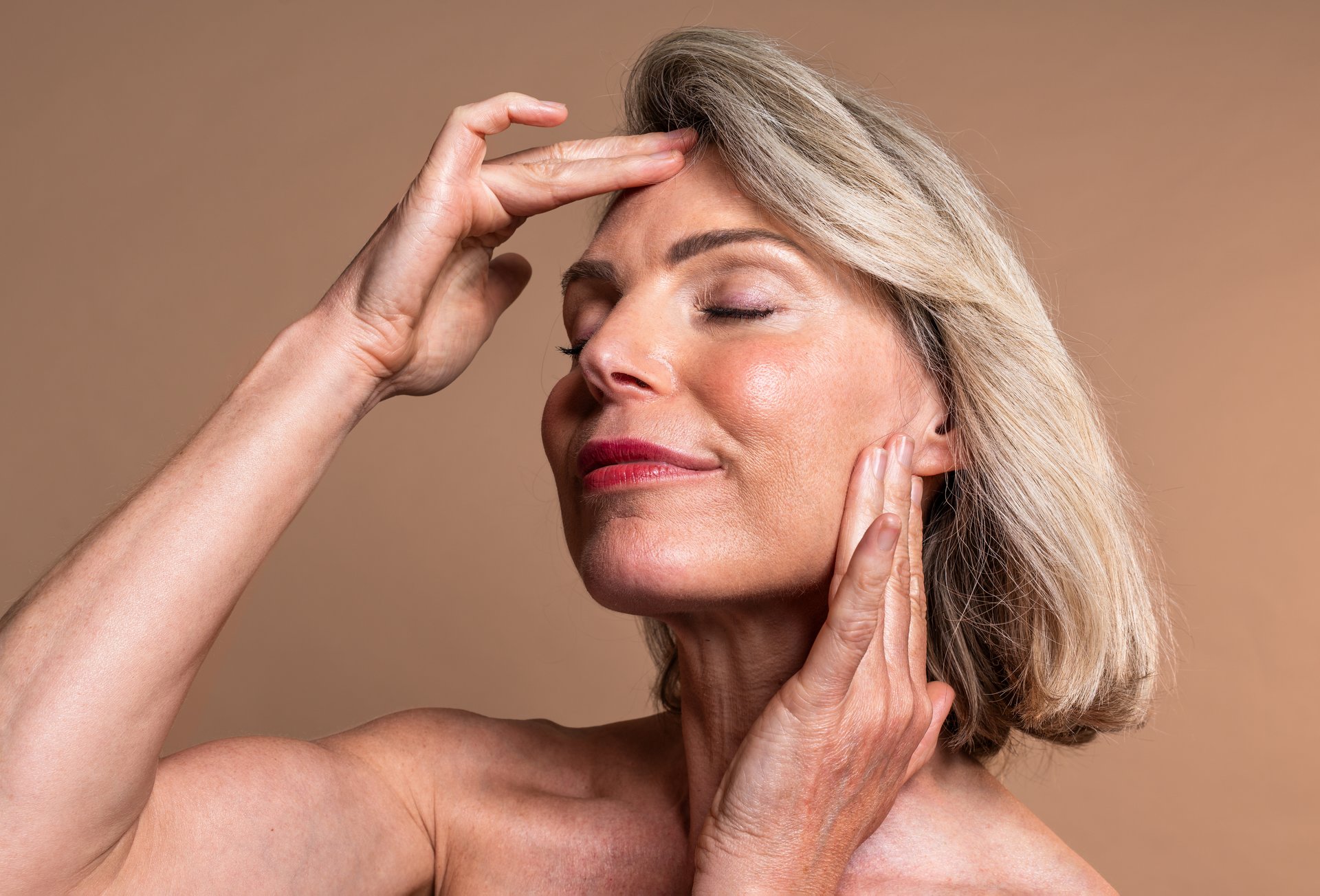 Beauty portrait of beautiful mature woman, concepts about cosmetics, skincare and wellness. Mature woman with closed eyes gently touching face, embodying graceful aging and radiant skin wellness