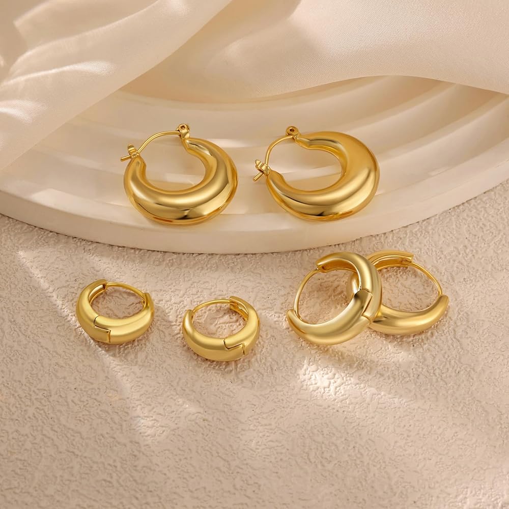 Gold hoop earrings of different sizes displayed on a textured surface with soft lighting.