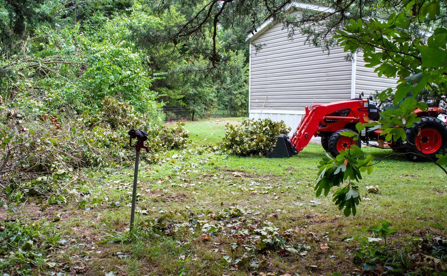 A tractor with scoop on the right side pushes brush to the left in a slow process of cleaning up downed trees in the backyard after a storm in Missouri.