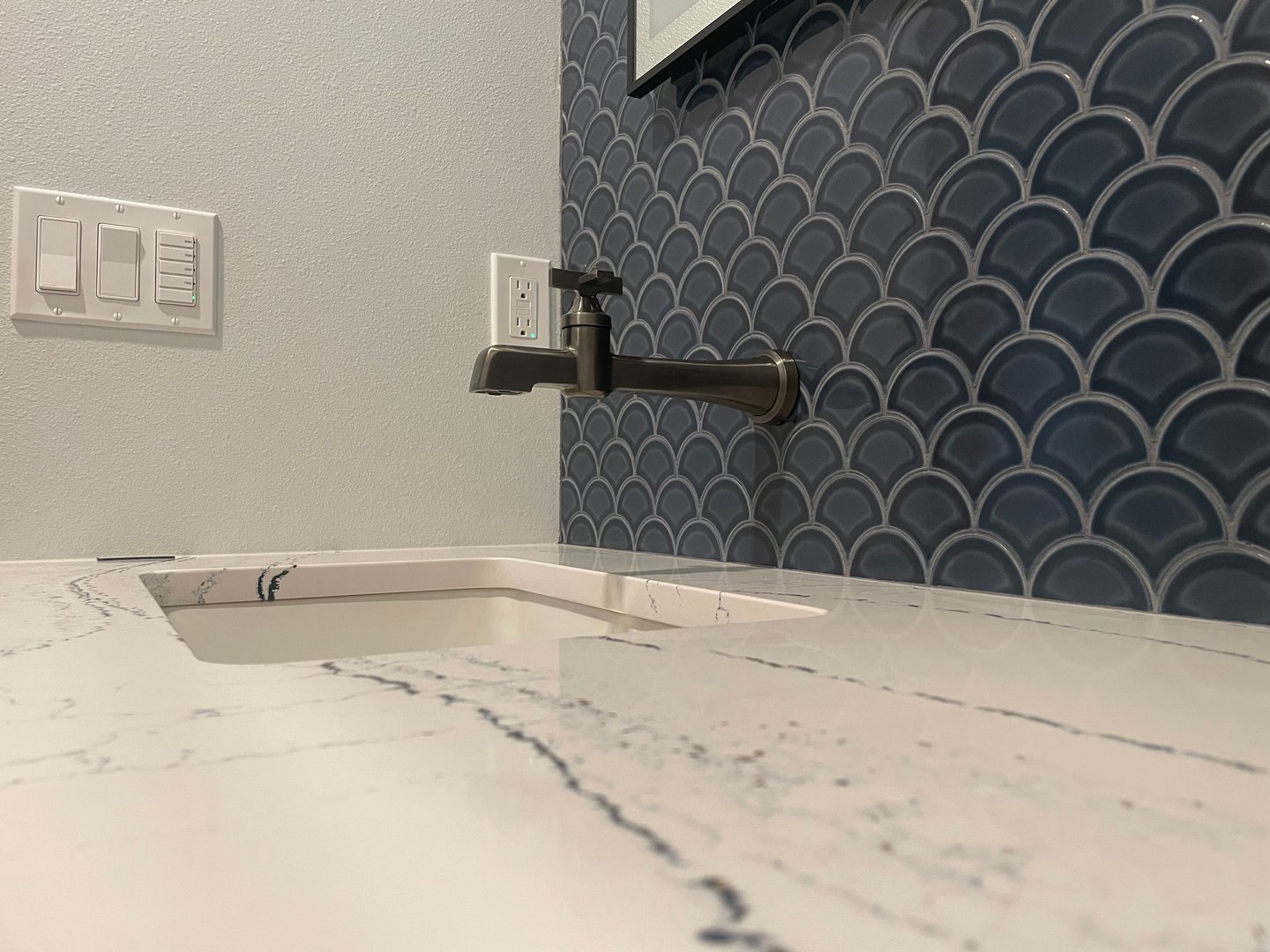 Modern bathroom sink with marble countertop, wall-mounted faucet, and blue scallop tile backsplash.
