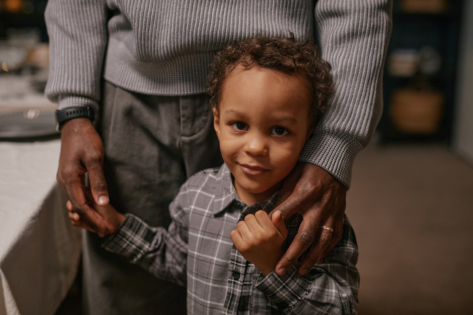 Portrait of cute smiling young boy in checkered shirt holding hands with elderly man while standing in living room during family reunion at home