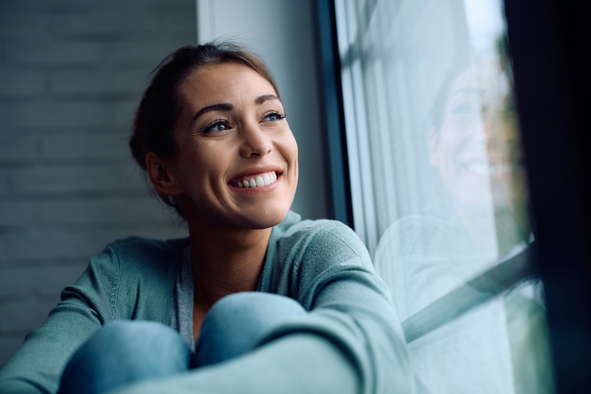 Smiling woman day dreaming while relaxing by the window at home. Copy space.