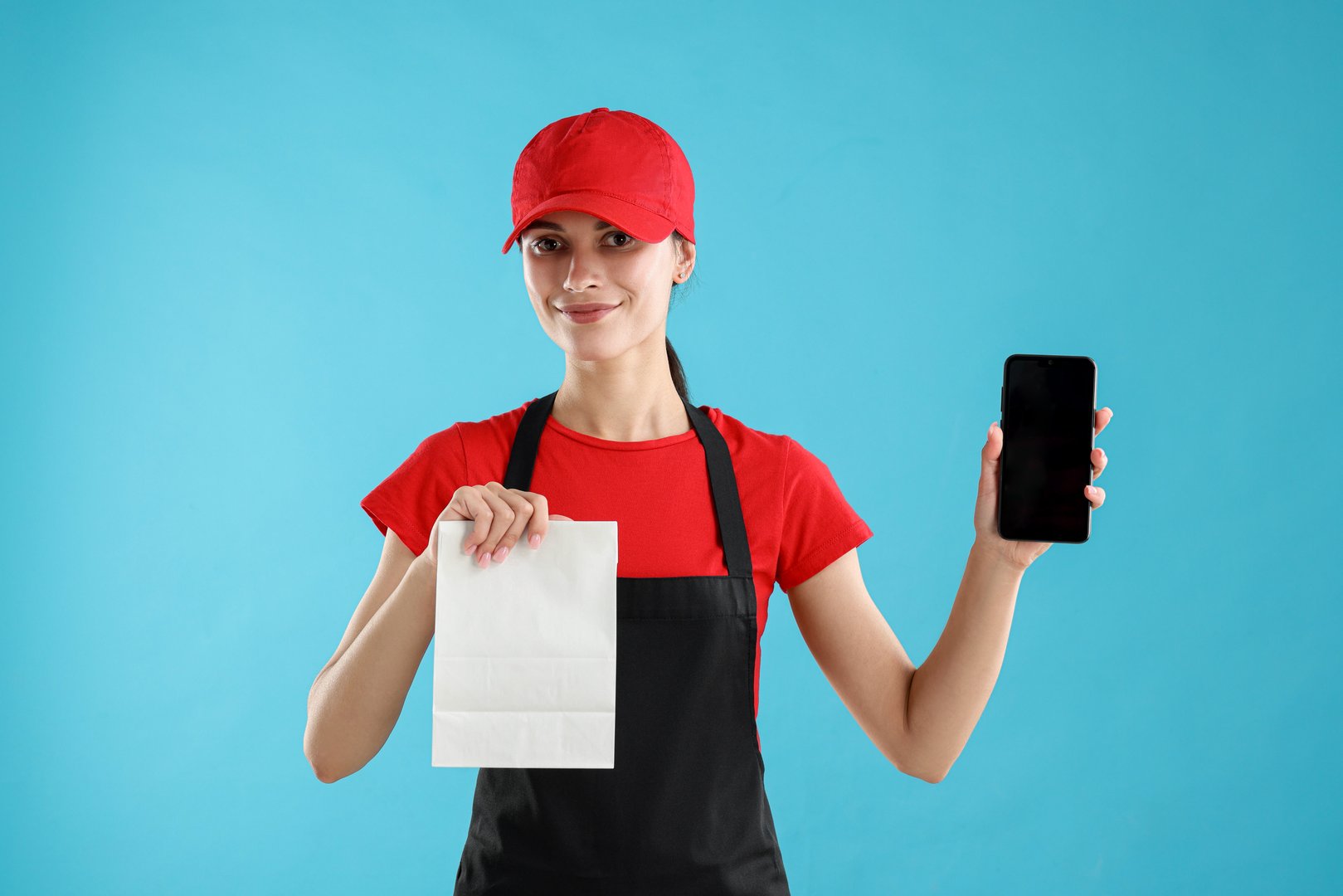 Fast-food worker with paper bag and smartphone on light blue background