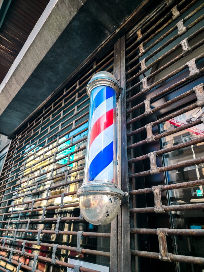 Close-up of traditional barber pole in Belgrade. Red, white, and blue spiral stripes on a vintage metallic fixture, symbol of classic barbershop culture and urban street style.
