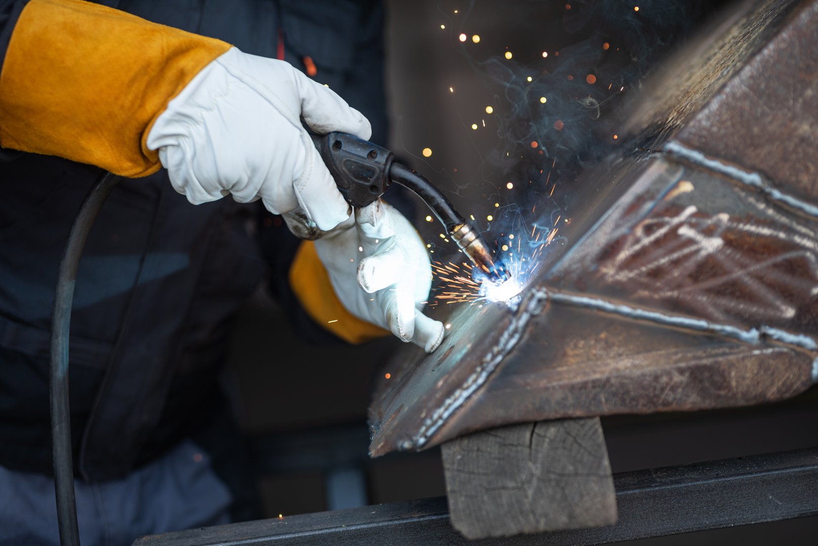 Welder is joining metal parts using mig mag welding technique with protective gloves in a workshop